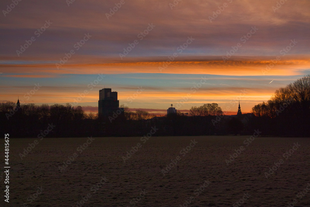 Naklejka premium Dunkle Parklandschaft bei Nacht mit Skyline-Silhouette von Leipzig und farbenfrohem Abendhimmel, Leipzig, Stadtkreis Leipzig, Sachsen, Deutschland