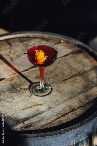 red Negroni boulevardier campari cocktail in hollow stem glass with orange peel rose on bourbon whiskey barrel in sun
