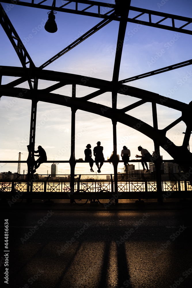 Unidentifiable backlit people enjoying the sunset sitting on a steel ...