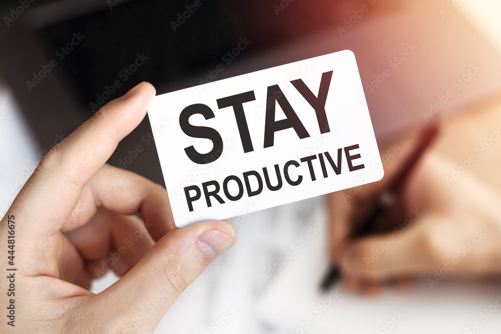 Close up of hand Business person keeps card with text STAY PRODUCTIVE. Document, pen and laptop. Close up of hand Business person keeps card with text STAY PRODUCTIVE. Document, pen and laptop.