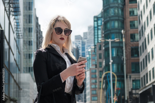 Young businesswoman wearing sunglasses is using her smartphone standing on the street. © Jorge Elizaquibel