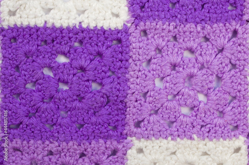 Woolen, knitted blanket. Consists of multi-colored squares knitted with woolen threads. The squares are purple, purple, white and sewn together. Textured image for the background. Close up.