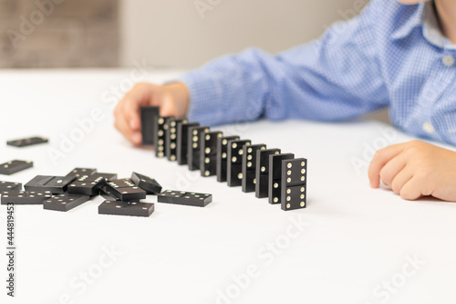 Six year old cute boy plays dominoes at home on a white wooden table. Selective focus. Close-up