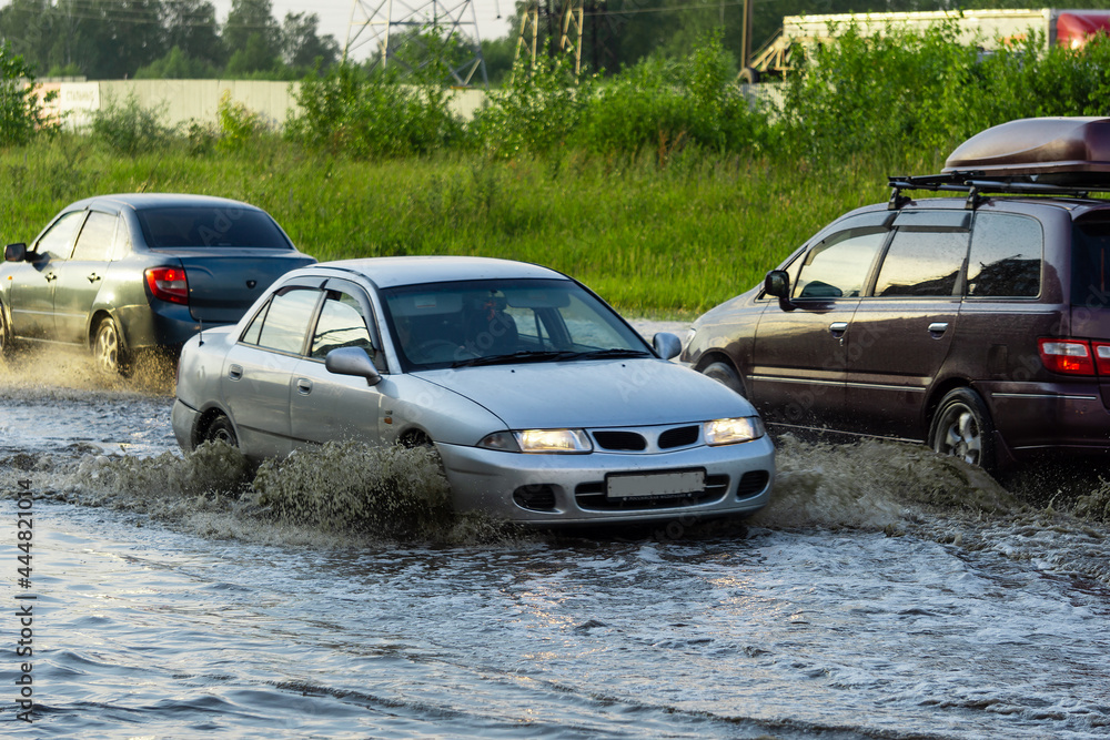 The car is driving through a deep puddle. Splashes are flying from under the wheels of the car. Flood in the city. The consequences of a downpour.
