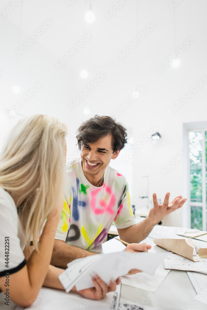 excited designer gesturing while talking to blonde colleague in fashion atelier excited designer gesturing while talking to blonde colleague in fashion atelier
