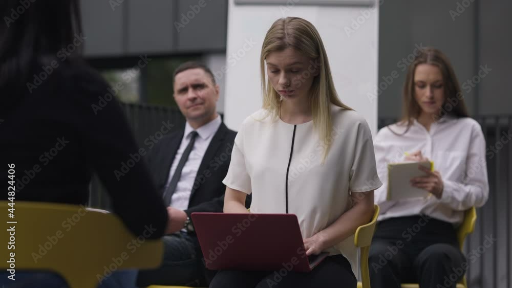 Concentrated secretary typing on laptop keyboard sitting with colleagues as spokesperson talking. Focused beautiful blond Caucasian woman recording meeting in slow motion. Business style concept Concentrated secretary typing on laptop keyboard sitting with colleagues as spokesperson talking. Focused beautiful blond Caucasian woman recording meeting in slow motion. Business style concept