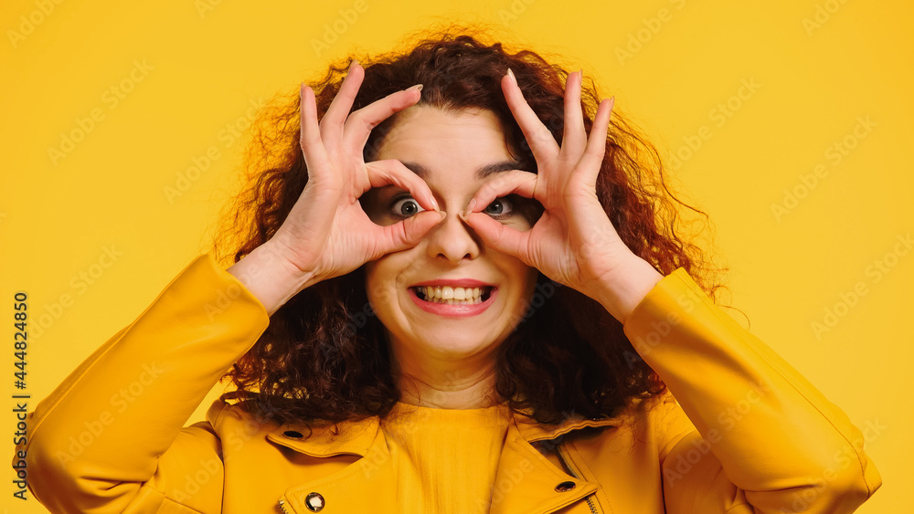 happy woman imitating eyeglasses with hands isolated on yellow happy woman imitating eyeglasses with hands isolated on yellow