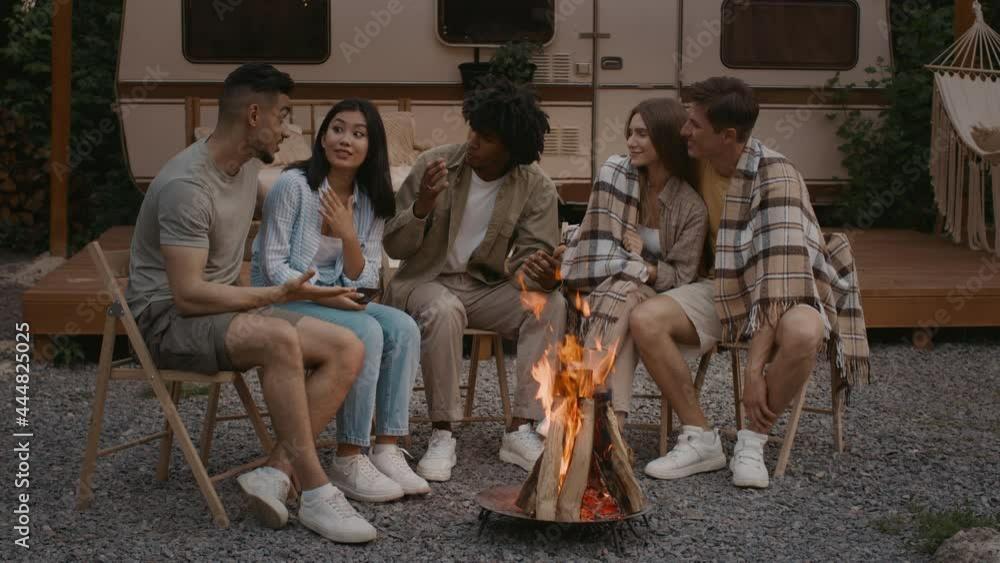 Group Of Multicultural Friends Sitting Around Bonfire At Camping And Chatting Group Of Multicultural Friends Sitting Around Bonfire At Camping And Chatting