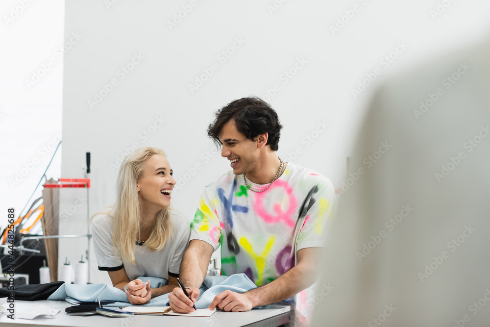 cheerful designers talking in atelier near samples of cloth and colors, blurred foreground cheerful designers talking in atelier near samples of cloth and colors, blurred foreground