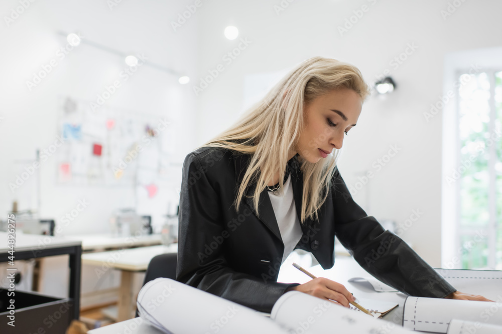 creative fashion designer writing in notebook near sewing patterns at workplace creative fashion designer writing in notebook near sewing patterns at workplace