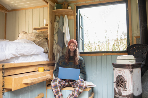 Portrait smiling young man using laptop in tiny cabin rental photo