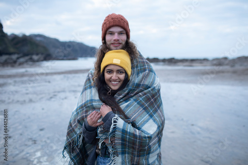 Portrait happy young couple wrapped in blanket on cold beach photo