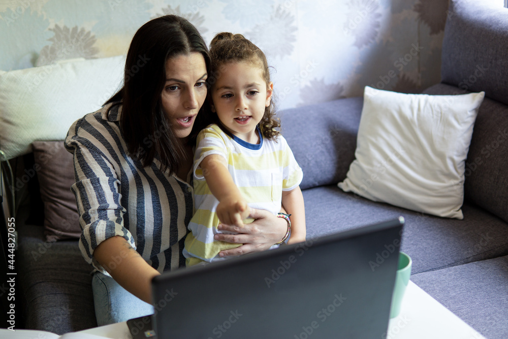 Young white Caucasian woman working from home with her son in her arms, with astonished face, pointing at the laptop screen Young white Caucasian woman working from home with her son in her arms, with astonished face, pointing at the laptop screen
