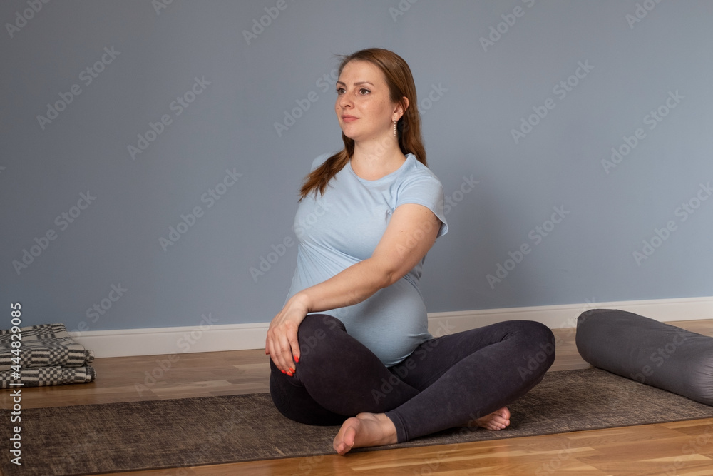 Pregnant caucasian woman sitting on floor in twisted pose stretching
