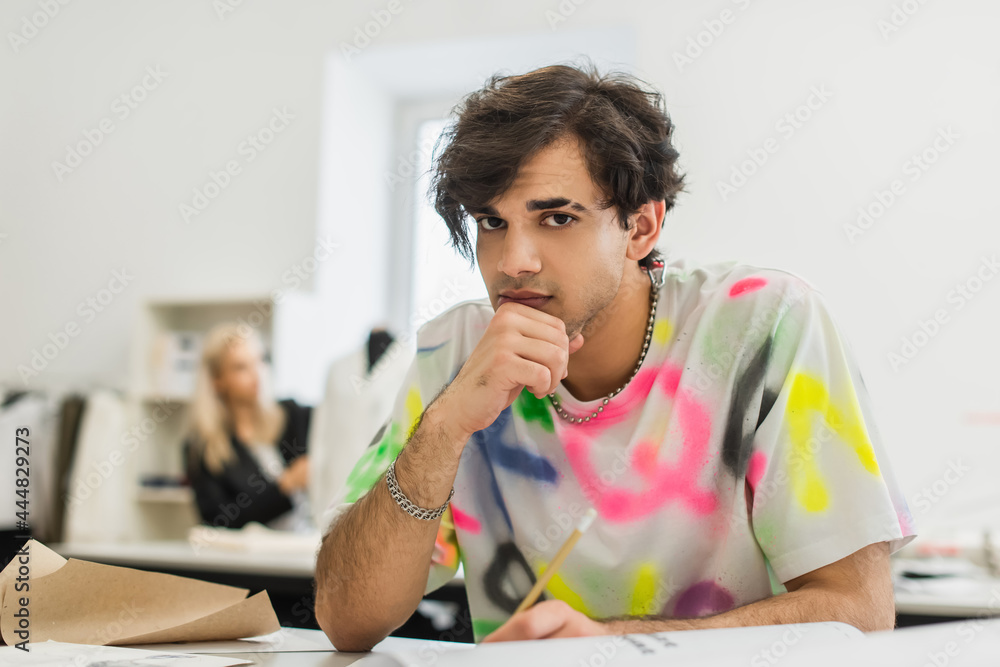 stylish fashion designer looking at camera while sitting at workplace near colleague on blurred background stylish fashion designer looking at camera while sitting at workplace near colleague on blurred background