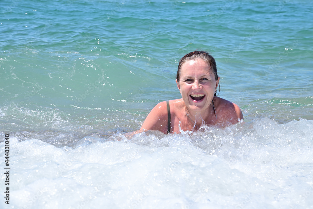 An adult attractive woman is swimming in the sea surf, she laughs with pleasure