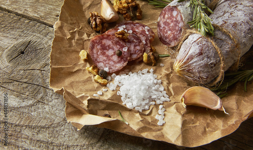 Italian salami wih sea salt, rosemary, garlic and nuts on paper. Rustic style. Close up.