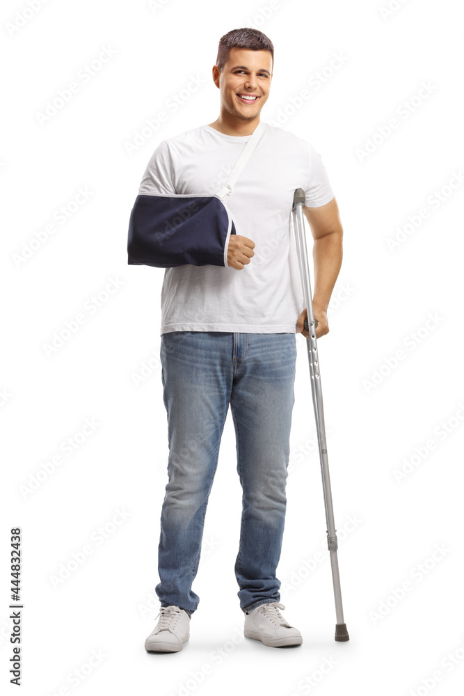 Full length portrait of a young man with a broken arm wearing an arm splint and standing with a crutch Full length portrait of a young man with a broken arm wearing an arm splint and standing with a crutch