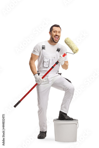 Full length portrait of a painter singing with a paint roller and standing on a bucket
