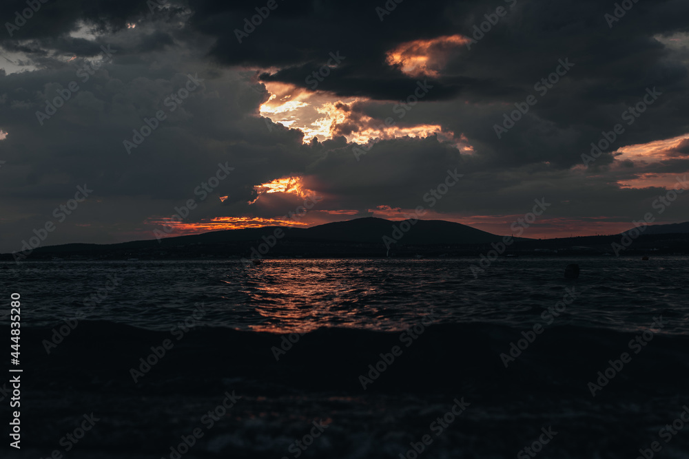 View of the sunset on the summer coastline on the Black Sea with silhouettes of mountains