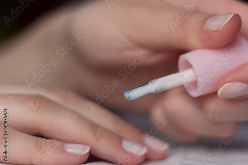 Closeup of a woman painting her own nails at home with a light pink nail polish.