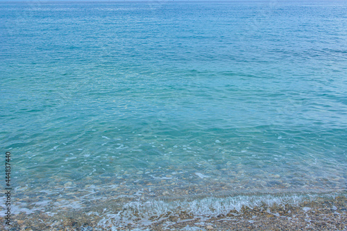 Soft wave of the turquoise sea on the tropical beach. Water surface background with copy space, pebble shore