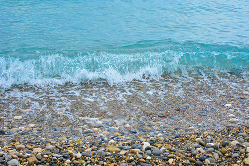 Soft wave of the turquoise sea on the tropical beach. Water surface background with copy space, pebble shore