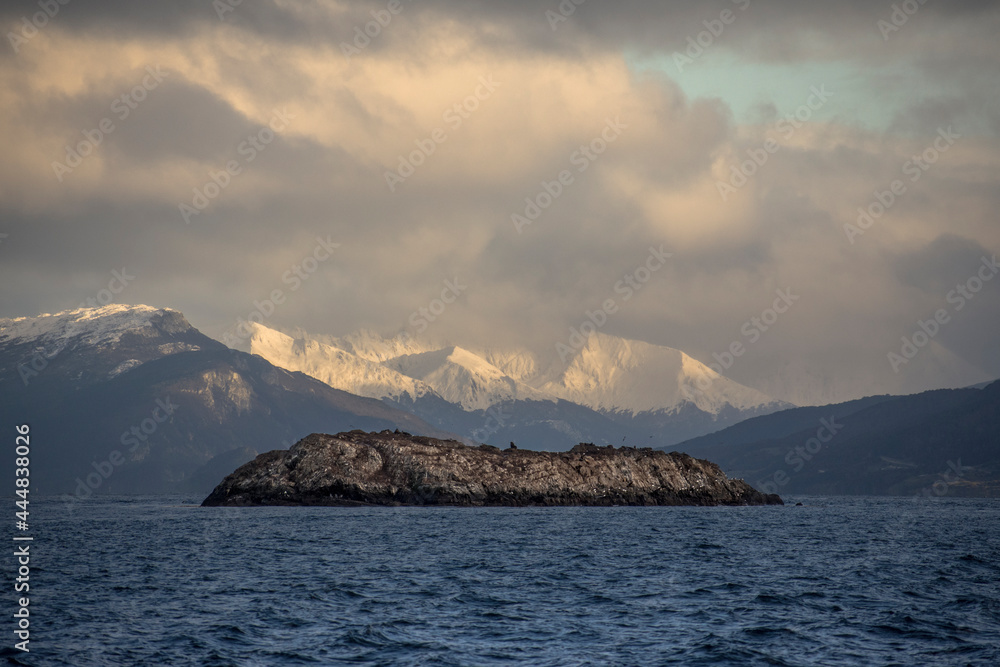 Centered photo of a little desertic island with sea animals and snowed Andes mountains with sunlight in the background in Ushuaia, Tierra del Fuego, Argentina Centered photo of a little desertic island with sea animals and snowed Andes mountains with sunlight in the background in Ushuaia, Tierra del Fuego, Argentina