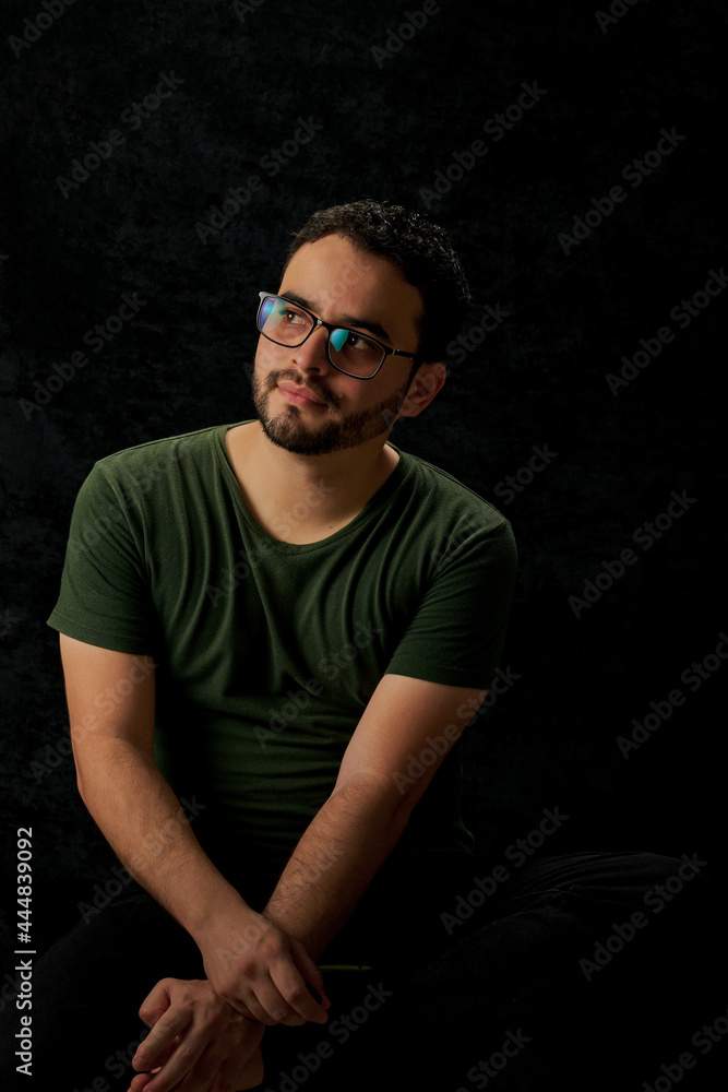 Hombre latino con gafas sentado pensando en un fondo negro Hombre latino con gafas sentado pensando en un fondo negro