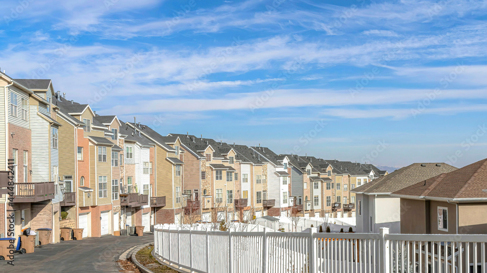 Pano Townhouses along road with white fence against scenic blue sky and white clouds