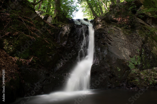 Small waterfall in Forsakar, Southern Sweden, surrounded by plants, shrubs, and bushes. Long-exposure shot.