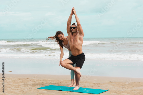 Couple practicing yoga together on the beach at the summer day.
