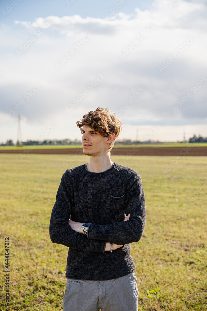 Portrait of a young handsome caucasian man with his arms folded in a grass field in the open air. Confident and thoughtful boy looks forward. Portrait of a young handsome caucasian man with his arms folded in a grass field in the open air. Confident and thoughtful boy looks forward.