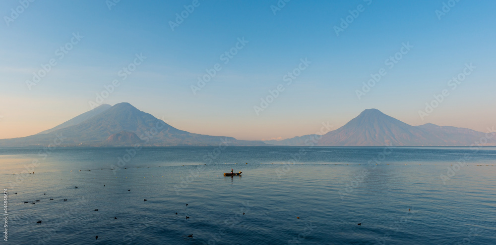Atitlan Lake panorama with maya indigenous man in fishing boat and volcano at sunrise, Panajachel, Guatemala.
