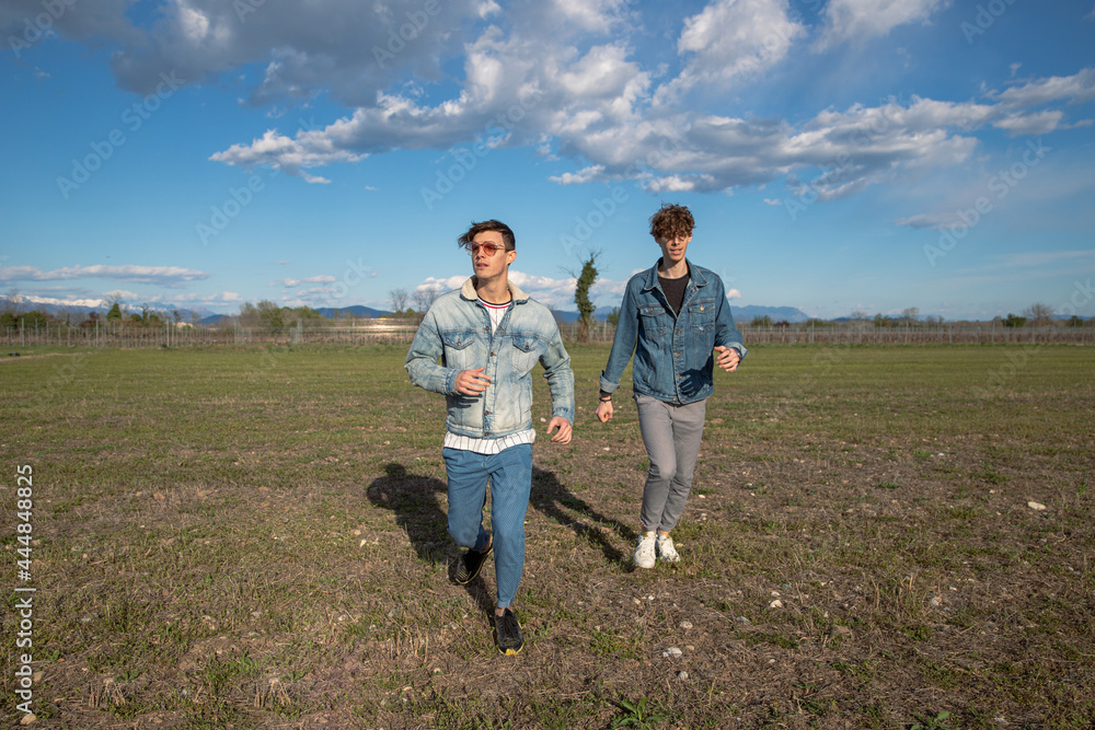 Two brothers run in a field of grass in the open air, young men dressed causally, wearing denim jackets. brotherhood concept