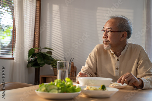 Unhappy Asian Senior older man sit alone  eat foods on table in house. 