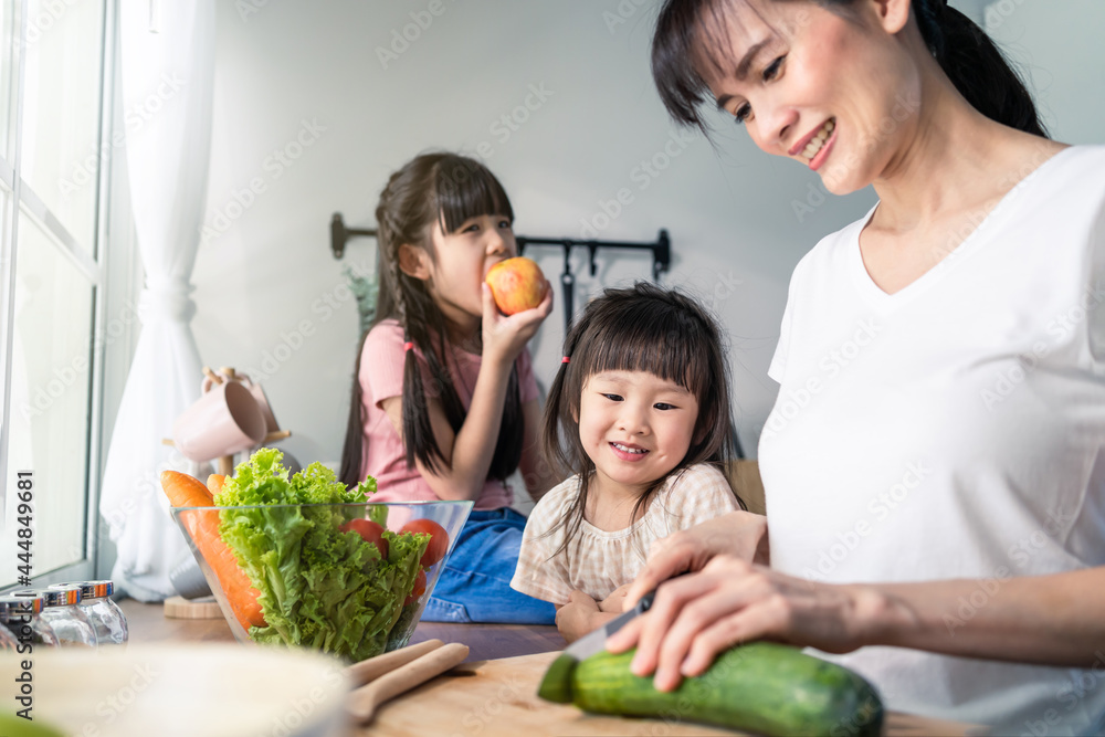 Asian beautiful mother cooking vegetable salad with two young daughter