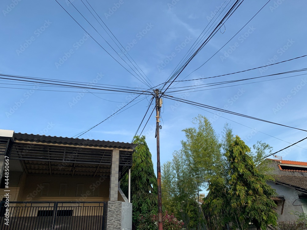 A power pole made of concrete is attached with lots of electrical wires and telephone wires.