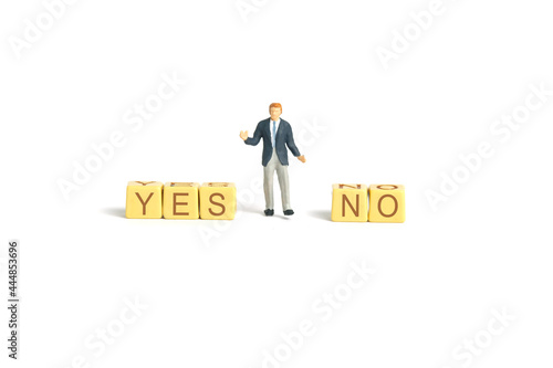 Miniature people toy figure photography. A shrugging businessman standing in the middle of yes and no  wooden cube block. Isolated on white background. Image photo