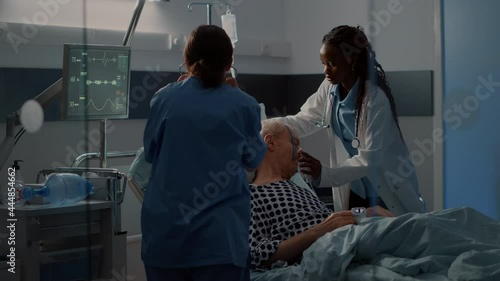 Patient with breathing problems in hospital ward bed needing reanimation help from nurse and african american doctor using oxygen tube. Old man with disease in intensive care room