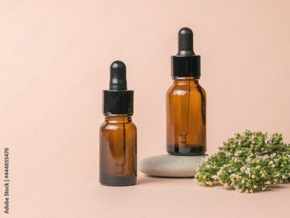 Two medical bottles, medicinal herbs and a stone on a beige background.