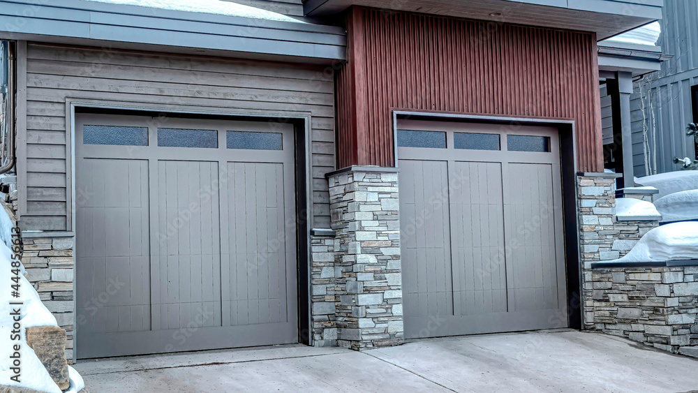 Pano Two car garage with glass paned gray doors at the facade of home in winter