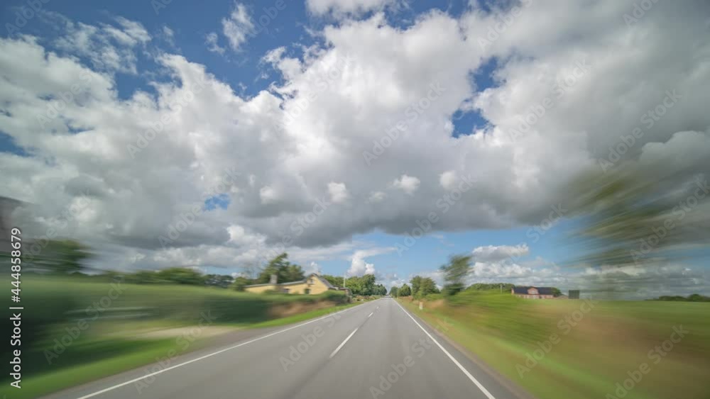 Dashcam view. Driving on the narrow two-lane rural road with heavy oncoming traffic through the villages and farm fields. Light fluffy clouds on a blue sky. Dashcam view. Driving on the narrow two-lane rural road with heavy oncoming traffic through the villages and farm fields. Light fluffy clouds on a blue sky.