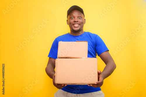 An African delivery or dispatch man with blue shirt carrying boxes and wearing a face cap