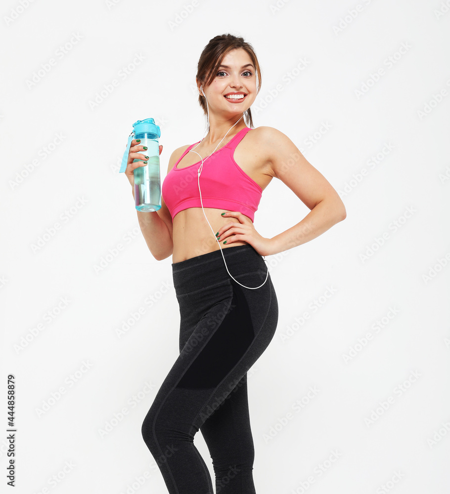 Sport, people and fitness concept: young woman wearing sport wear holding a bottle with water over white background Sport, people and fitness concept: young woman wearing sport wear holding a bottle with water over white background