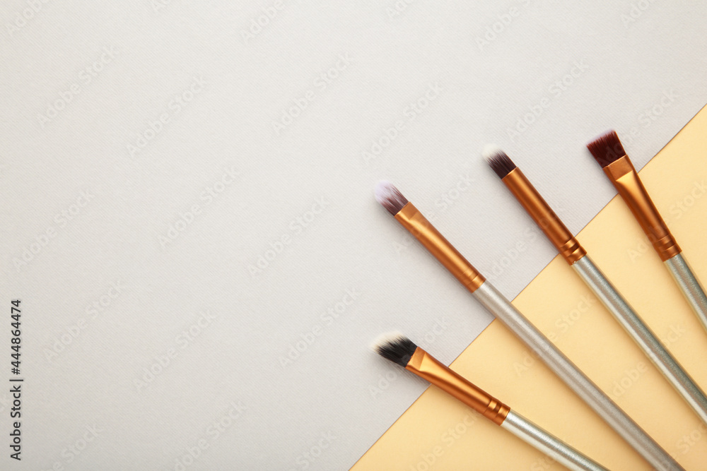 Various makeup brushes on grey and beige background with copy space. Various makeup brushes on grey and beige background with copy space.