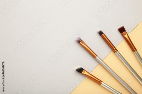 Various makeup brushes on grey and beige background with copy space.
