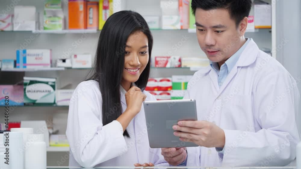 Portraits of pharmacist male and female checking drug in pharmacy store at hospital. Asian doctor checking medicine data from tablet and wearing medical coat. Shelves pharmacy background in drugstore. Portraits of pharmacist male and female checking drug in pharmacy store at hospital. Asian doctor checking medicine data from tablet and wearing medical coat. Shelves pharmacy background in drugstore.