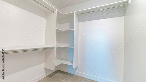 Pano Interior of a walk in closet with shelves and clothes rod mounted on white wall