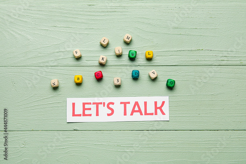 Paper with text LET'S TALK and cubes on color wooden background